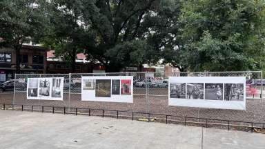 White banners with photograpy line a fence.
