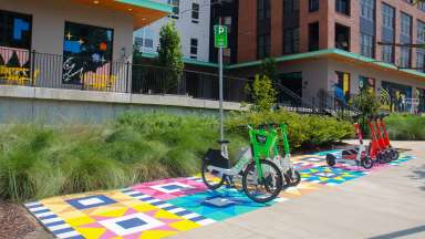 Bright green scooters are parked on a pavement painted with a colorful quilt square design.