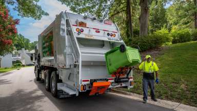 A service worker collects a yard waste bin at the back of a Solid Waste Services truck.