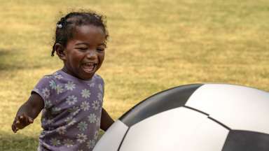 a child smiling and playing with an oversized soccerball