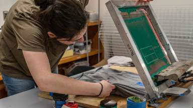 A student positions a t-shirt under their screen printing screen.