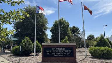 Wilders Grove Solid Waste Services Facility sign and flags on a clear, sunny day.