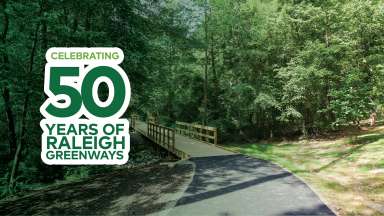 a photo of a paved greenway trail and bridge with a badge that says "Celebrating 50 years of Raleigh Greenways"
