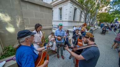 people playing instruments and singing on a sidewalk