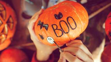 a person painting black cats and bats on a small orange pumpkin