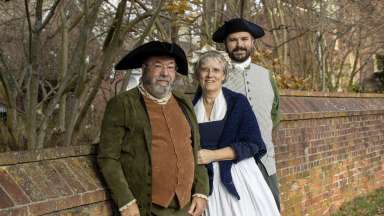 the musical trio Ampersand wearing colonial attire standing outside in front of a brick wall