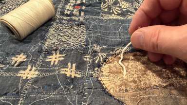 A hand pulls thread through a stitched piece of denim.