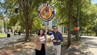 Two City of Raleigh employees stand under the "Fourth Ward Entertainment District" sign