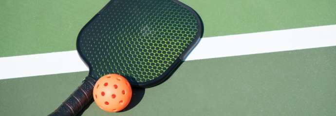 Pickleball paddle and ball laying on a court stripe