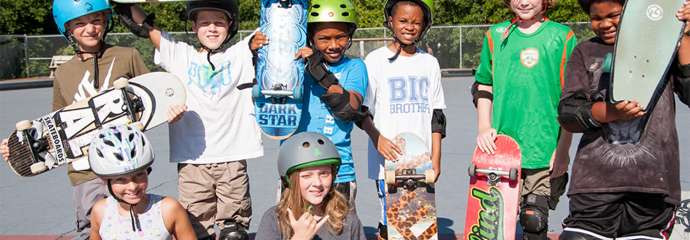 teens wearing helmets, holding skateboards while smiling