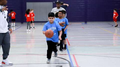 A group of kids playing basketball while a young boy dribbles the ball