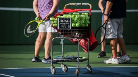 Tennis balls in cart with players in background