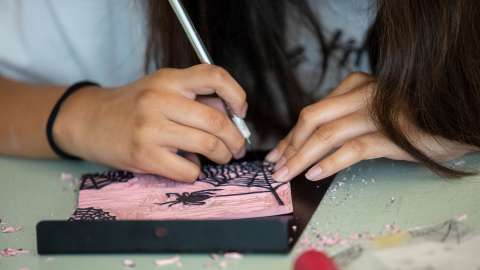 A teen etches into a pink block to be used for printing
