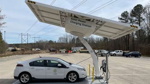 A City car sits under a large panel marked as &quot;Solar Power Charging Station&quot;