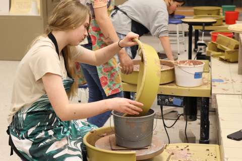 Teen artist bending over a potter's wheel to mold clay.