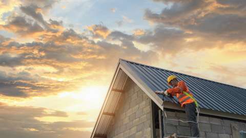 Man on ladder fixing roof on a house with sunset clouds in background