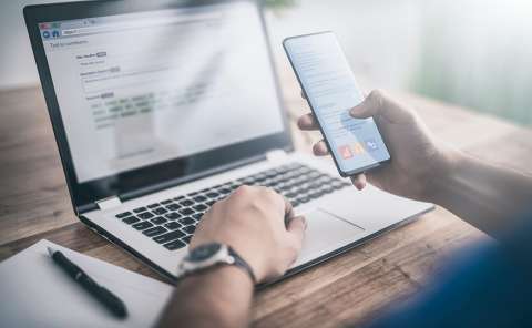 Person using a phone while working with a laptop.