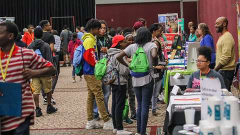 From the 2019 Raleigh Youth Summit youth are mingling around a large room talking to exhibitors at tables about different topics.