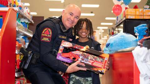 A police office and a young boy hold a toy and smile at the camera.