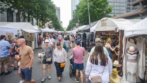 Street lined on both sides with vendor tents, crowd walking down street and browsing in tents.