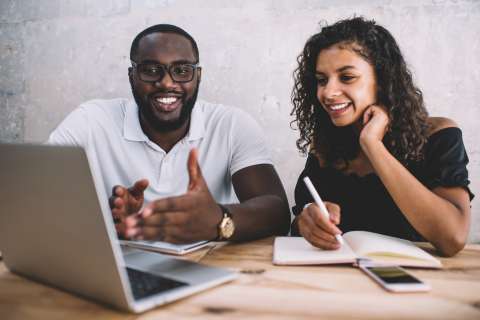 Man and woman viewing laptop screen and taking notes