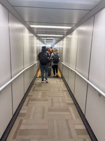 Looking down a jetway of a plane with passengers pulling luggage
