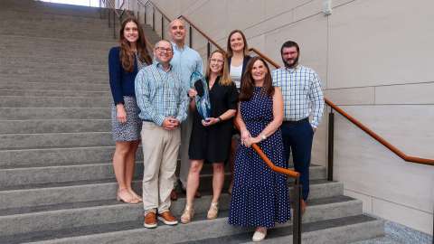 Employees of the Raleigh Convention Center pose with award on stairs at the convention center