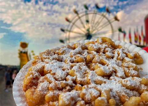 Funnel cake with powdered sugar with blurred fair games in the background