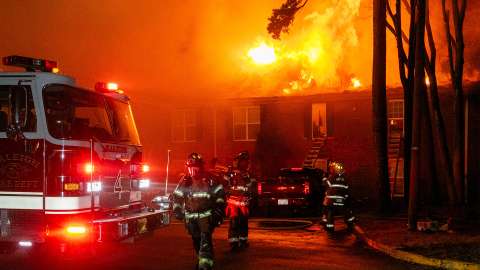 A brick apartment building on fire with a fire truck with two firefighters in front