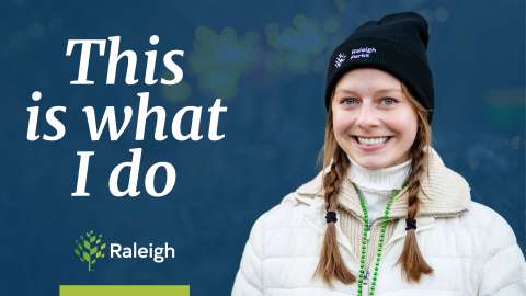 A woman with a Raleigh Parks beanie and a winter jacket on with green beads around her neck. The words "This is what I do" with the Raleigh logo over a blue background