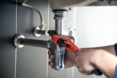 Hand repair under sink leak with red wrench