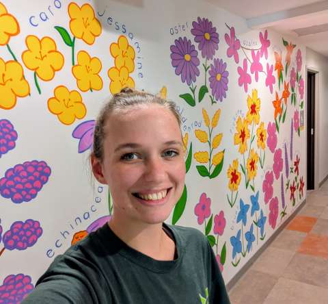 The artist stands in front of her wildflower mural
