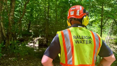 Worker stands looking at Turkey Creek with yellow "Raleigh Water" vest on