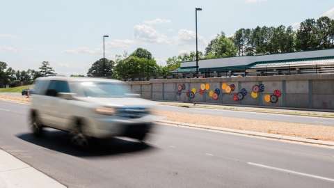 Colorful discs line a wall along a roadway where a vehicle drives past