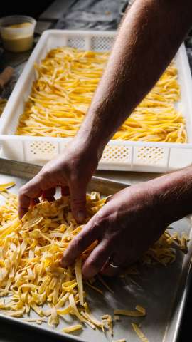 Two trays of handmade pasta fill the image with two hands moving the pasta within the lower tray