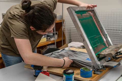 A student positions a t-shirt under their screen printing screen.