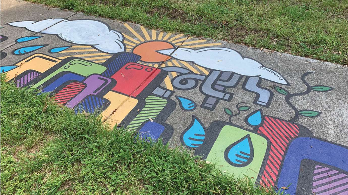 A storm drain and sidewalk mural on North Hills Drive with colorful buildings and rain show the affects from water pollution 