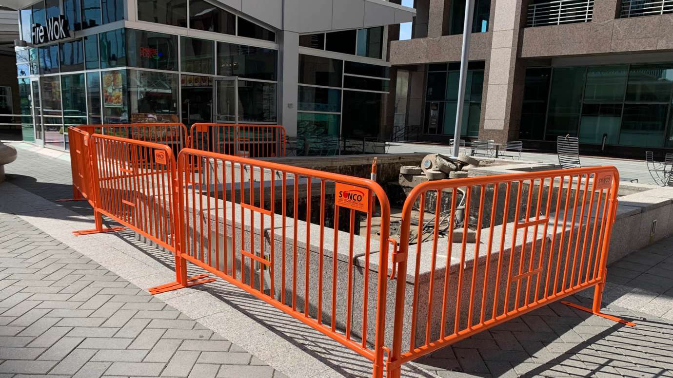 An orange metal construction fence around planters in City Plaza that are being repaired