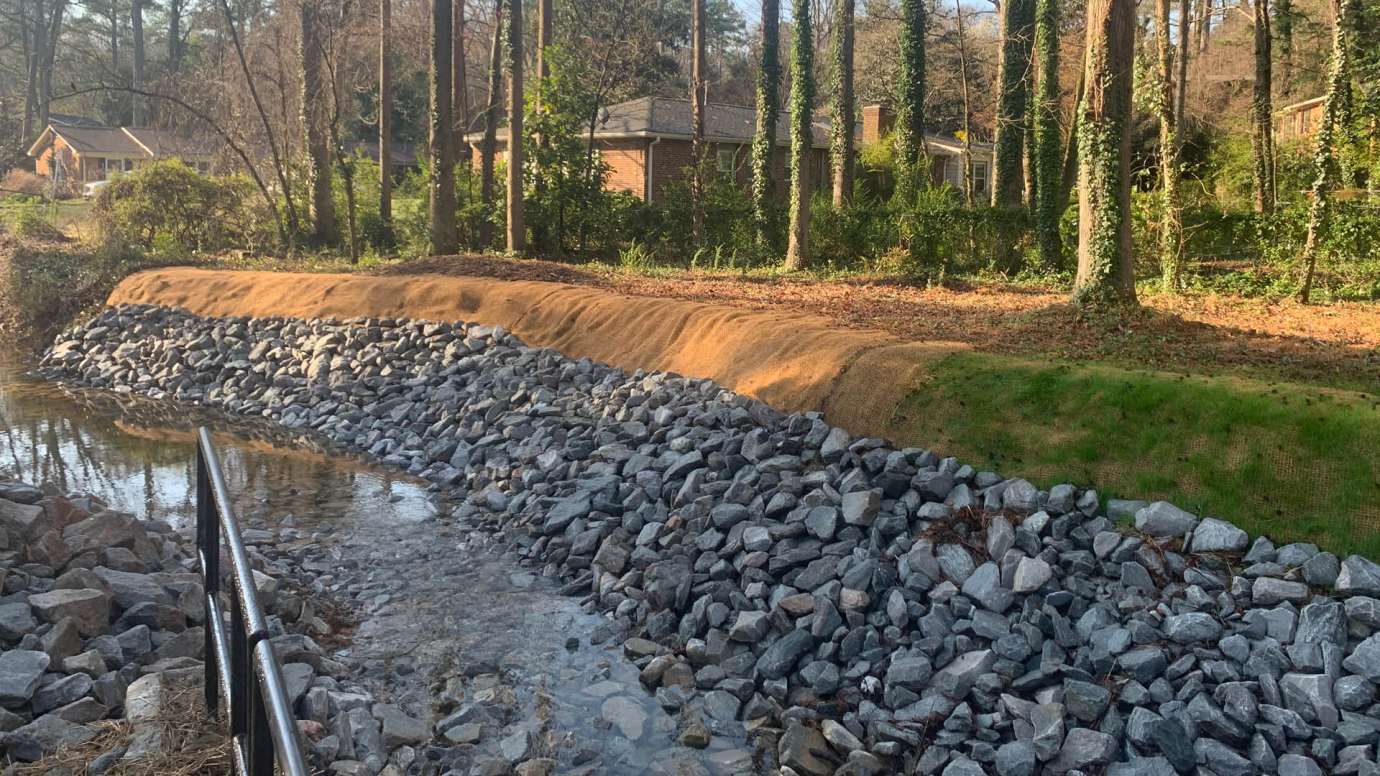 A stream on Swift Drive with repaired streambanks and rock to protect the stream.