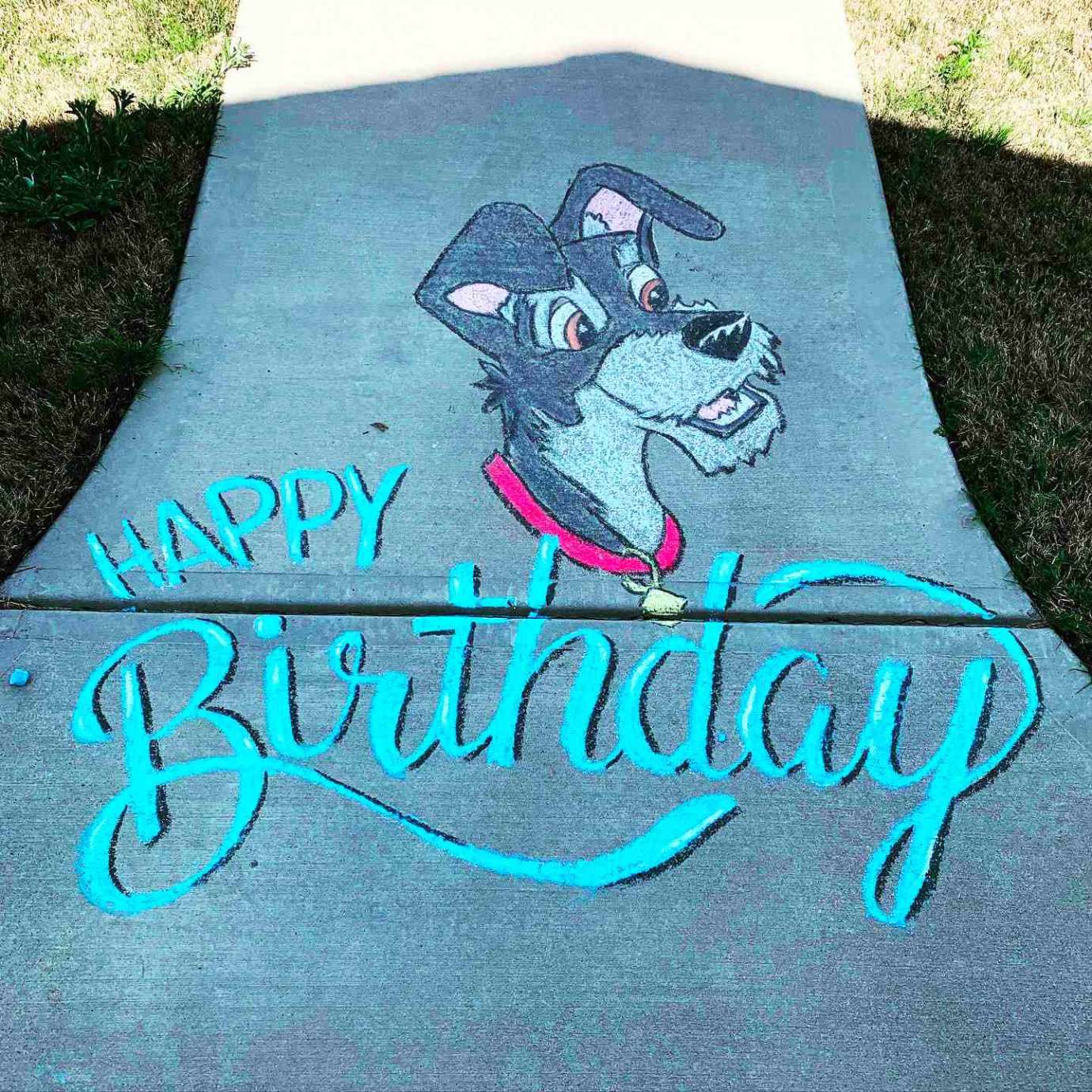 A sidewalk chalk drawing of the Disney dog character, Tramp, and the words "Happy Birthday"