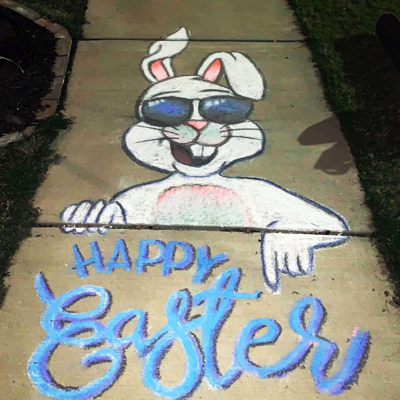 A sidewalk chalk drawing of a white rabbit with sunglasses on and the words "Happy Easter"