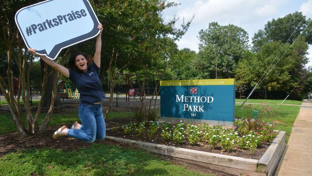 Praks staff jumping in front of Method Road Park sign holding Parks Praise sign