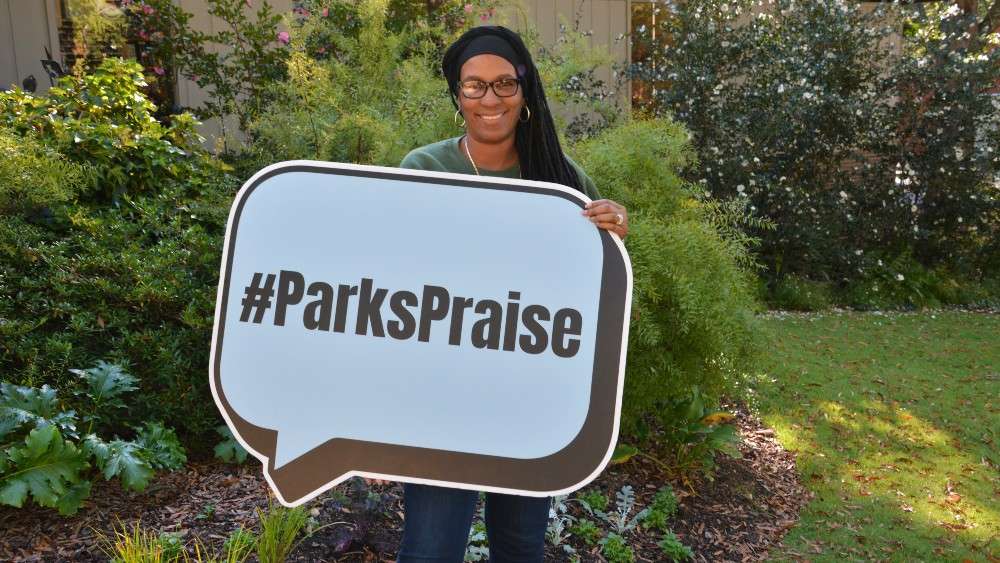 Parks staff holding Parks Praise sign and smiling in front of plants