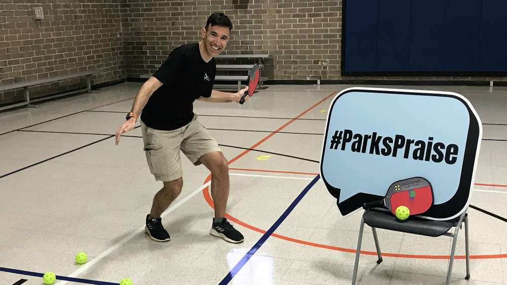 Parks staff holding pickleball paddle by parks praise sign