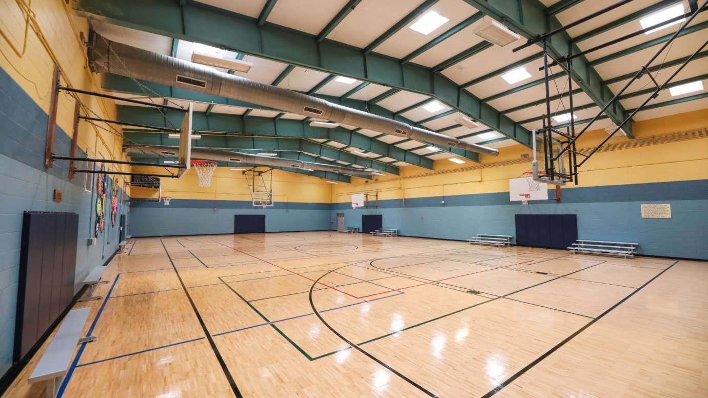 A large open gymnasium with multiple hoops and bleachers 