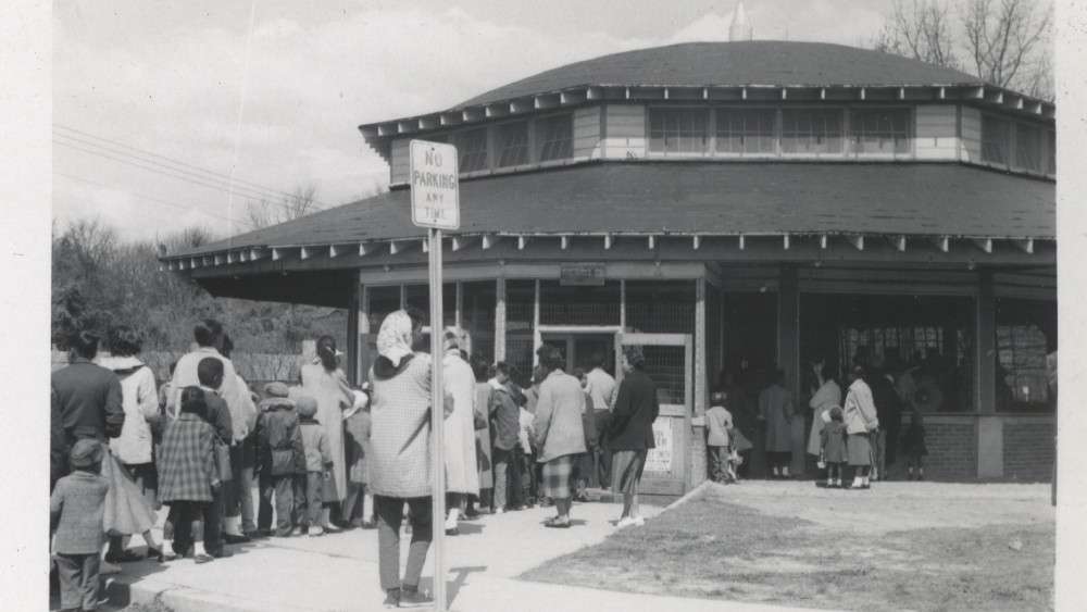 Black and white historic image of old carousel house with people in line to ride