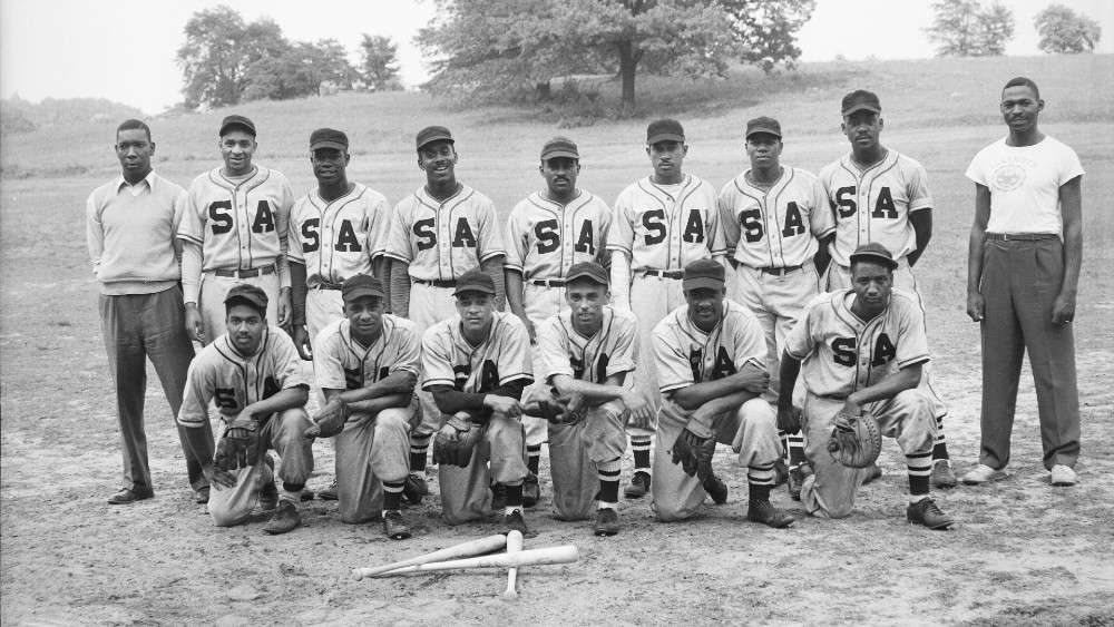 Historic image of baseball team lined up in two rows with bats in front