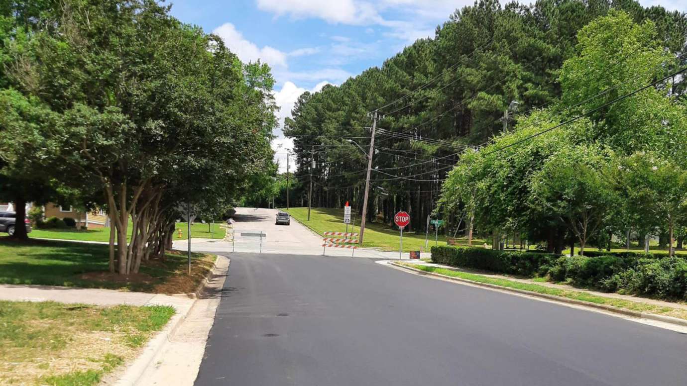 Newly paved part of Bragg Street on a sunny day with green trees lining the road. 