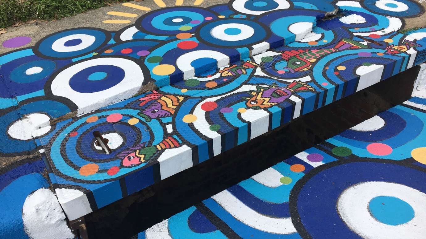 A sidewalk mural covering a storm drain that features interconnected circles in different shades of blue and white and small colorful striped fish