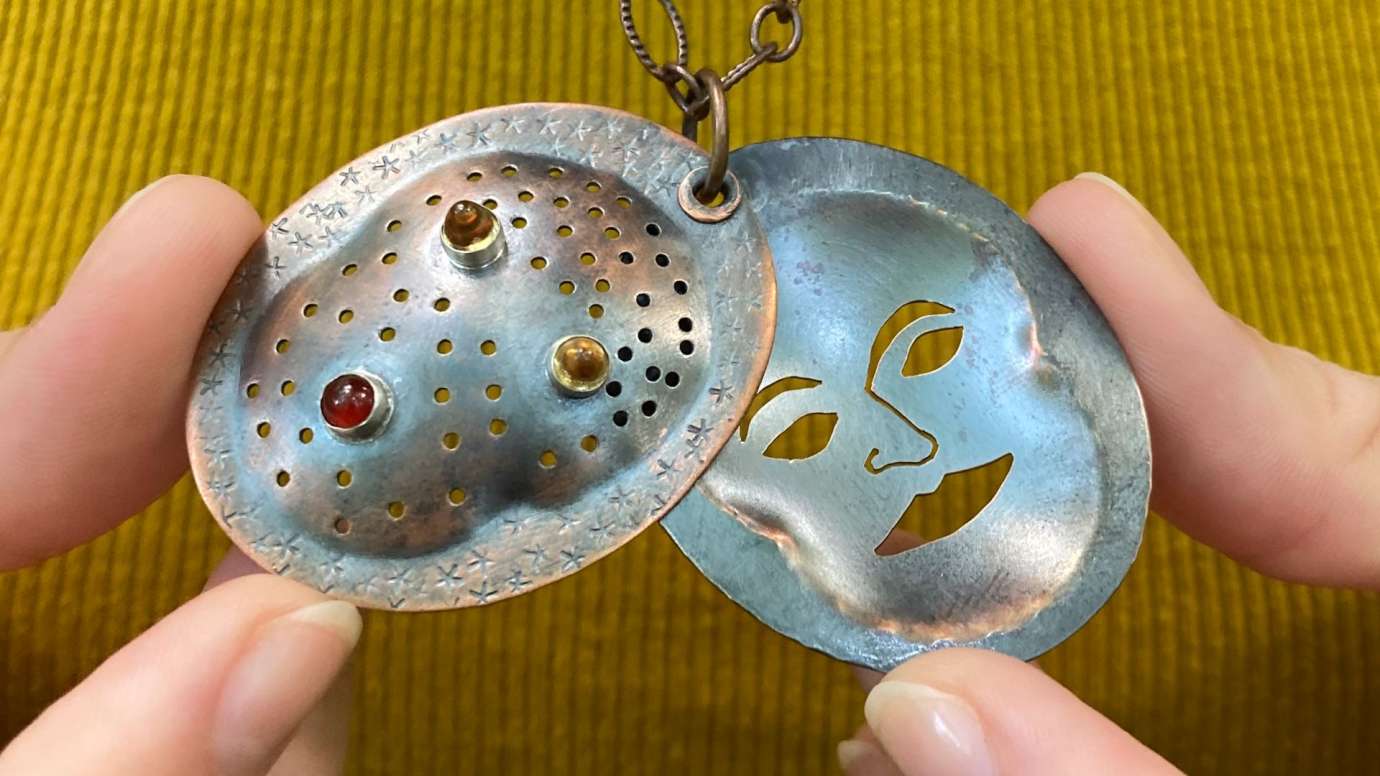 A detailed image of a locket necklace with a face on it by artist Amy Veatch